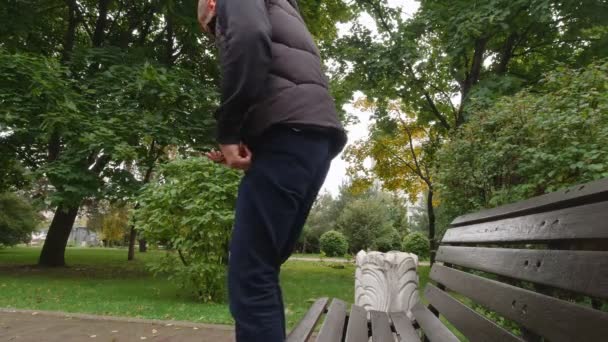 Um homem com um telefone senta-se em um banco — Vídeo de Stock