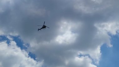 Arka planda gökyüzü bulutlarında helikopter uçuyor.