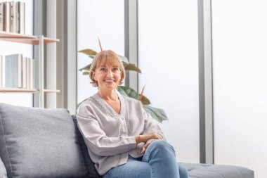 Evdeki kanepede oturmuş gülümseyen olgun bir kadının portresi oturma odasındaki rahat rahat yaşlı bir kadını rahatlatıyor.