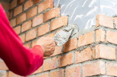 Duvara beton yapıştıran işçinin eli tuğla, harç ve macun bıçağıyla duvar ören inşaat işçisi. 