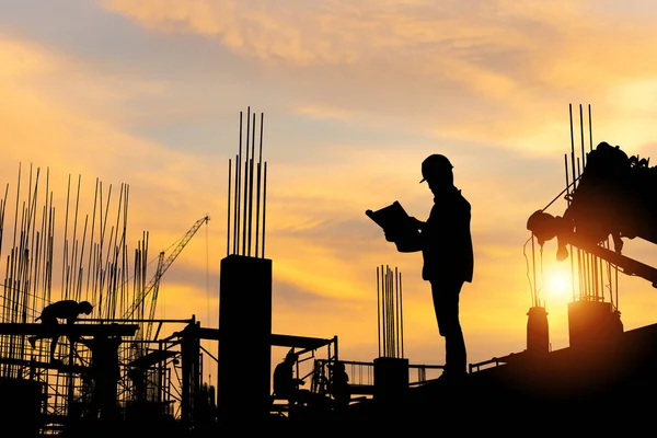 現場でプロジェクトをチェックするエンジニアと労働者のシルエット 建設現場の労働者チーム夕方の日没時間 — ストック写真