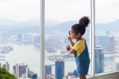 Penceresinden dışarı bakan büyüteçle küçük bir kız çocuğu dikilip pencereden bakan bir çocuk.