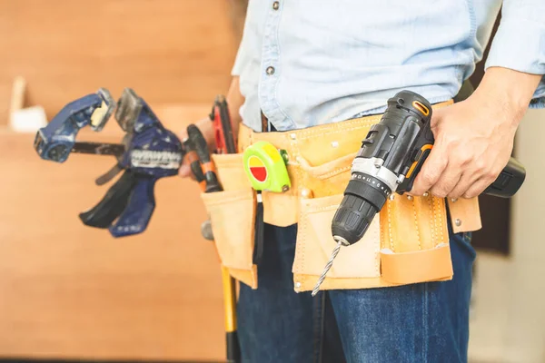 Alet kemeri takan, elinde matkap tutan marangoz ahşap atölyesinde ekipmanla çalışan marangozluk yapan adam.
