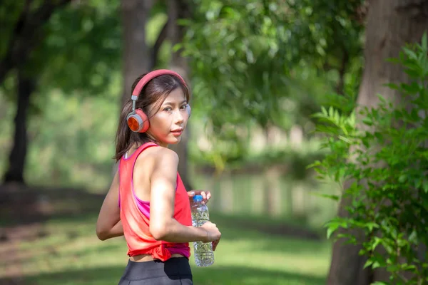 头戴耳机 头戴水瓶的年轻漂亮女子 回头看相机 运动女子 在夏季绿园 — 图库照片
