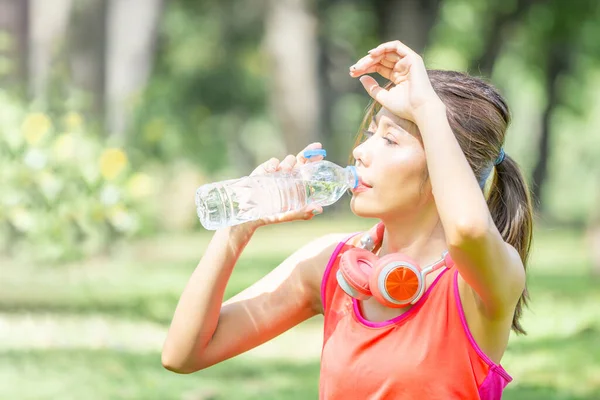 Yeşil Park 'ta plastik şişeden su içen genç ve güzel bir sporcu kadın spor yaptıktan sonra su içiyor.