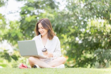 Yeşil bir parkta dizüstü bilgisayarla oturan genç bir serbest yazar. Neşeli, modern bir kadın parkta oturmuş kahvesini yudumluyor ve dizüstü bilgisayarına bakıyor.