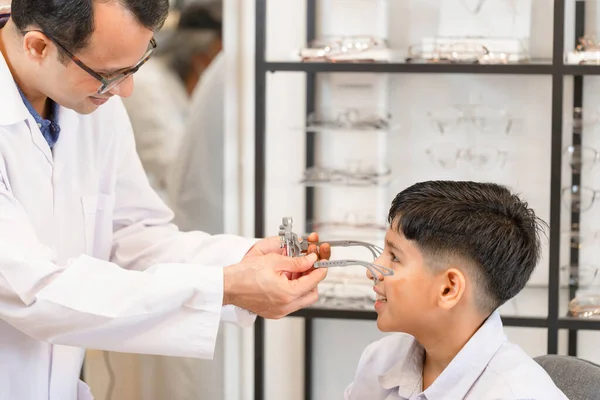 Boy choosing eyeglasses frames and talking with ophthalmologist in optical store, Child doing eye test checking examination with optometrist in optical shop, Family buy glasses