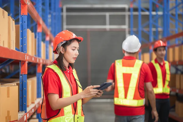 Female factory manager using digital tablet in a warehouse, Warehouse workers group in aisle between rows of tall shelves full of packed boxes