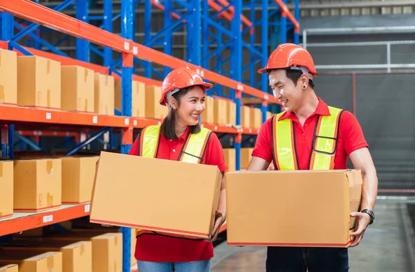 Male and female workers in hardhat holding cardboard box walking through in retail warehouse, Warehouse worker working in factory warehouse