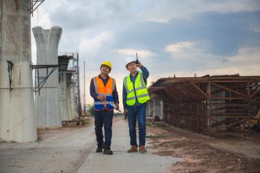 Engineer and foreman worker checking project at building site, Engineer and builders in hardhats discussing blueprint on construction site, Teamwork concepts