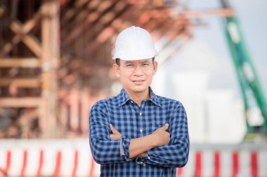 Worker man with arm crossed looking at camera, Engineer checking project at building site, Man in hardhat at infrastructure construction site
