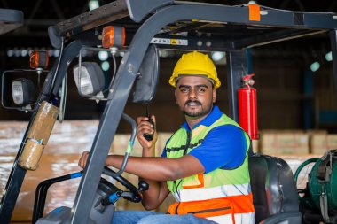 Depo forklift yükleyicisi mallarla çalışır, kasklı ve güvenli yelek giyen işçi kutuları yüklemek için forklift kullanır.