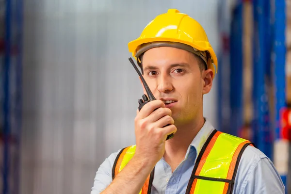 Foreman in hardhat safety vest with Two-Way radio working in logistics center, Warehouse worker man working in factory warehouse industry and using radio talking communication