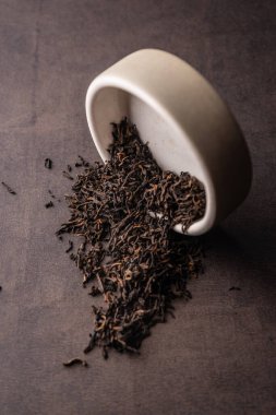 Seçici odaklanma, doğal siyah yaprak çayı. Kil kasesinde demleniyor. Dikey açı, makro. Karanlık bir arka planda. Menüler ve kafeler için