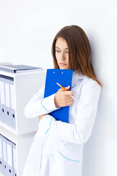 Portrait of pensive young female doctor holding clipboard in hos — Stock Photo, Image