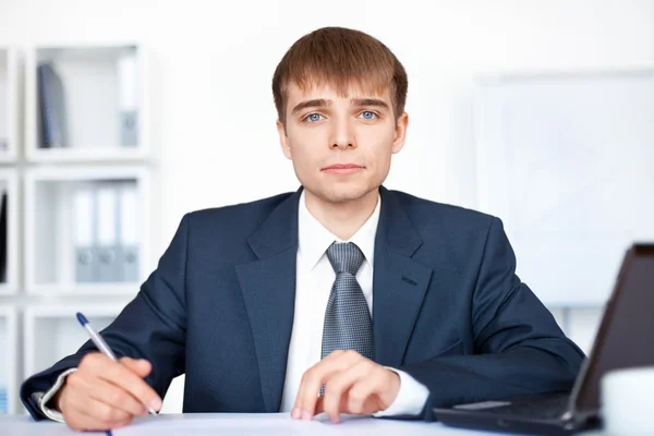 Portret van jonge lachende zakenman schrijven op papierwerk in o — Stockfoto