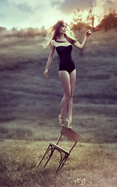 Beautiful girl balances on back of chair outdoors. — Stockfoto