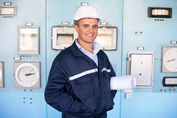 Giovane ingegnere con casco e cianografie nella sala di controllo — Foto Stock