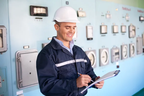 Jovem engenheiro sorrindo tomar notas na sala de controle — Fotografia de Stock