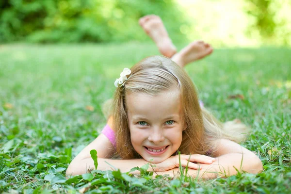 Красивая маленькая девочка лежит на зеленой траве — стоковое фото