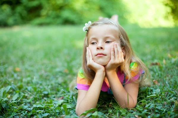 Schönes kleines Mädchen liegt auf dem grünen Gras — Stockfoto