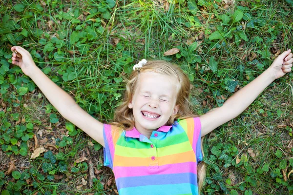 Little funny girl with closed eye lying on grass — Stock Photo, Image