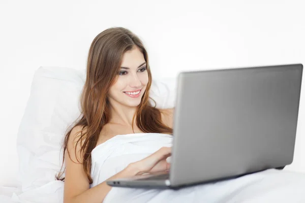 Mooie jonge vrouw met laptop op bed — Stockfoto