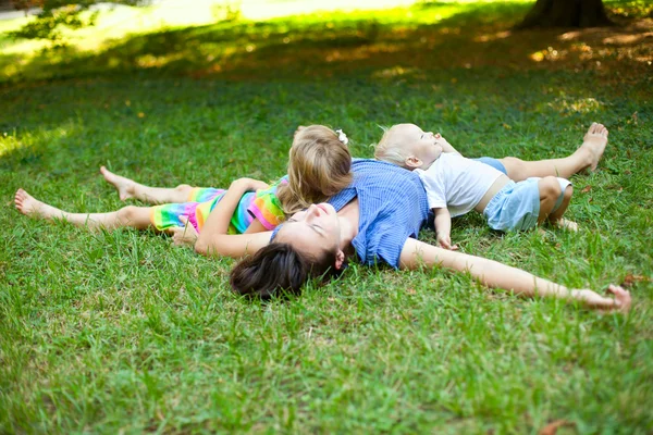 Joyful family enjoying themselves laying on the grass in park — Stock Photo, Image