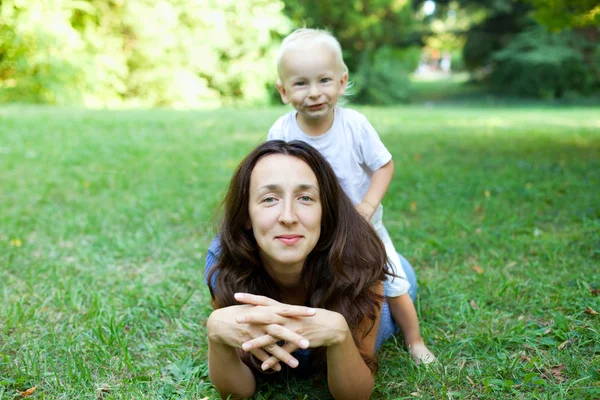 Retrato de uma mãe deitada no gramado com o filho sentado em h — Fotografia de Stock