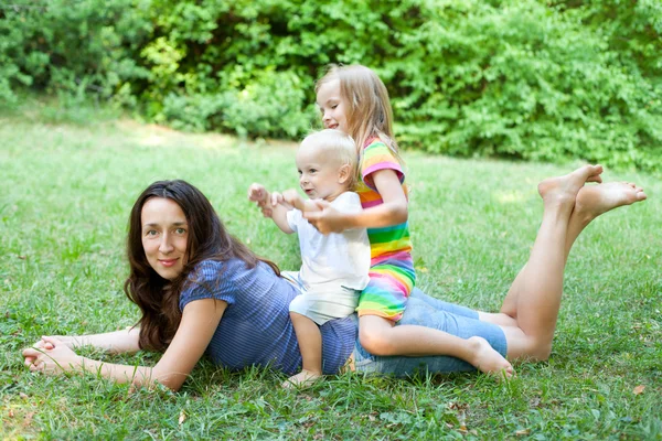 Portrait of a young mother lying on the lawn with her children s — Stock Photo, Image