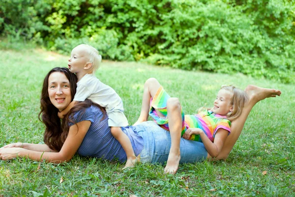 Portrait of a young mother lying on the lawn with her children s — Stock Photo, Image