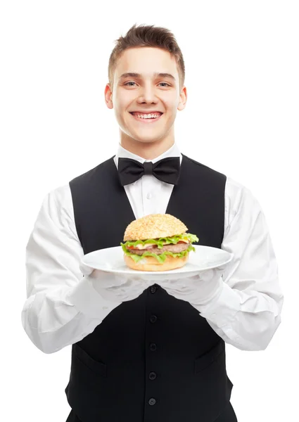 Giovane felice cameriere sorridente che tiene hamburger sul piatto — Foto Stock