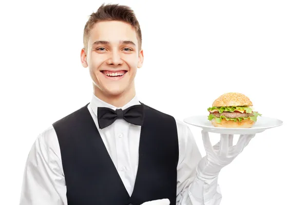 Joven camarero sonriente sosteniendo hamburguesa en el plato — Foto de Stock