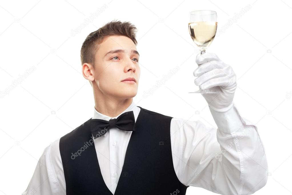 Young waiter looking at the glass filled with white wine