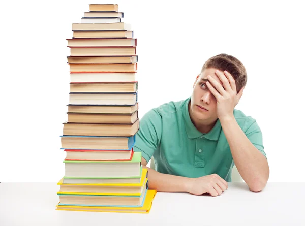Estudiante frustrado sentado en el escritorio con la pila de libros altos — Foto de Stock