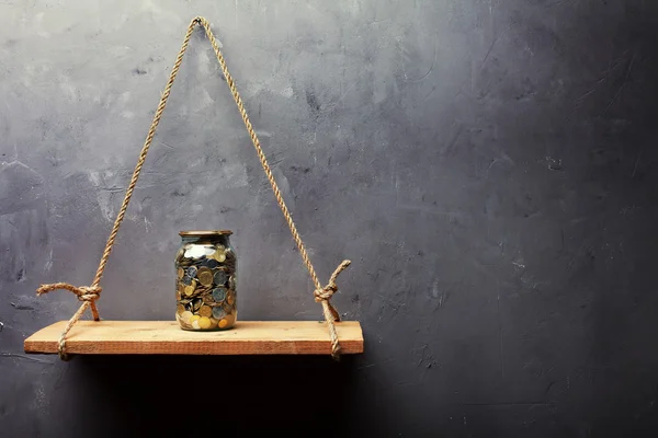 Glazen pot met munten op de oude houten plank — Stockfoto