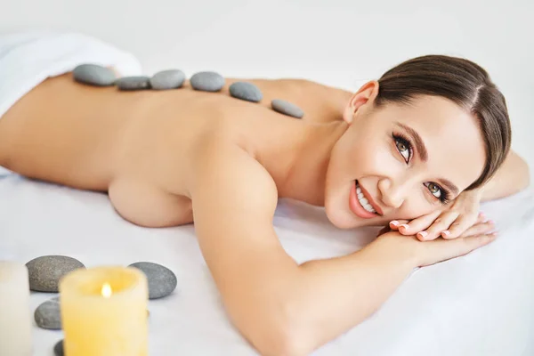 Mladá žena relaxuje v lázeňském salonu s horkými kameny na zádech — Stock fotografie
