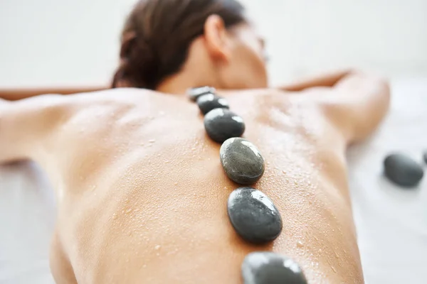 Beskuren närbild kvinna avkopplande i spa salong med heta stenar på ryggen — Stockfoto