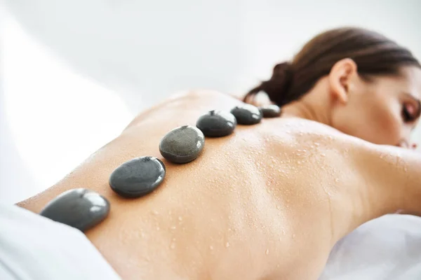Young female relaxing in spa salon with hot stones on her back — Stock Photo, Image