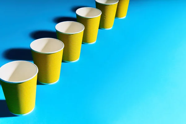 Perspectiva atenuante de la taza de papel amarillo en fila sobre fondo azul con espacio para copiar —  Fotos de Stock