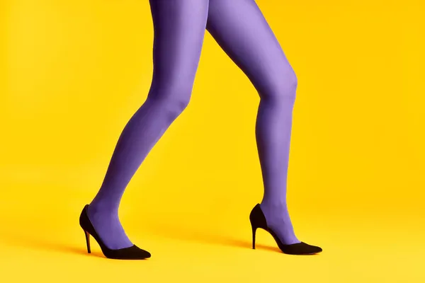 Female legs in purple tights and high heels shoes on yellow background — Stock Photo, Image