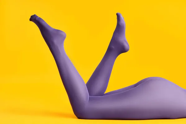Schlanke Beine der schönen jungen Frau in leuchtend lila Strumpfhosen entspannen auf gelbem Hintergrund — Stockfoto
