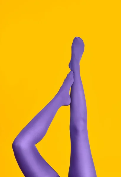 Slim piernas femeninas en mallas púrpuras levantadas sobre fondo amarillo —  Fotos de Stock