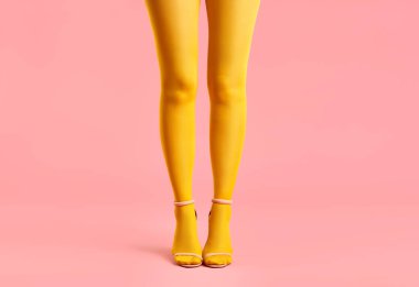 Sarı taytlı uzun ince bacaklar ve pembe arka planda şık yüksek topuklu ayakkabılar..