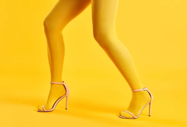 Largas piernas delgadas de mujer joven en medias amarillas y zapatos de tacón alto elegantes posando sobre fondo amarillo —  Fotos de Stock