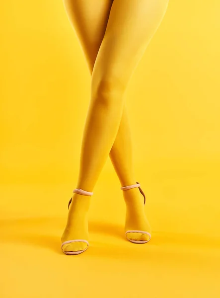 Dlouhé štíhlé zkřížené nohy mladé ženy ve žlutých punčochách pózovat na žlutém pozadí — Stock fotografie