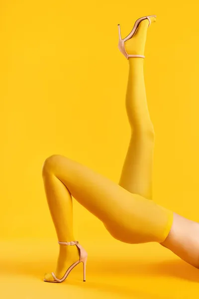 Kaki panjang tipis wanita muda dengan celana kuning dan sepatu hak tinggi bergaya dengan latar belakang kuning. — Stok Foto