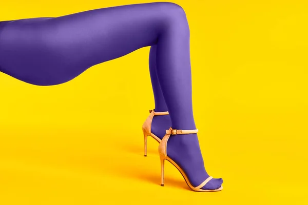 Lange schlanke Beine einer jungen Frau in lila Strumpfhosen und stylischen High Heels auf gelbem Hintergrund. — Stockfoto
