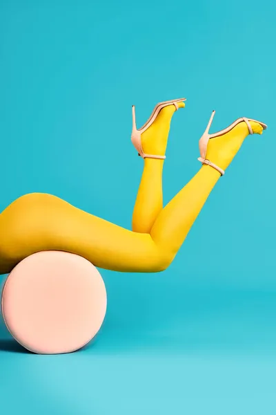 Beine einer schönen jungen Frau in leuchtend gelben Strumpfhosen und Stöckelschuhen auf Hocker liegend — Stockfoto
