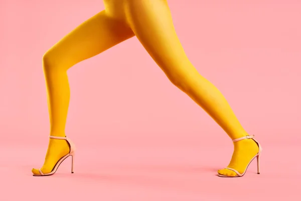 Profilo vista di gambe di bella giovane donna che indossa collant luminosi camminare su sfondo rosa — Foto Stock